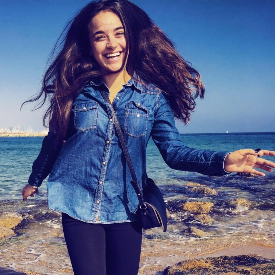 photo of a young woman in jean shirt smiling an jumping at the beach